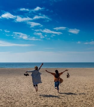 Two people run on a beach, their arms outstretched.