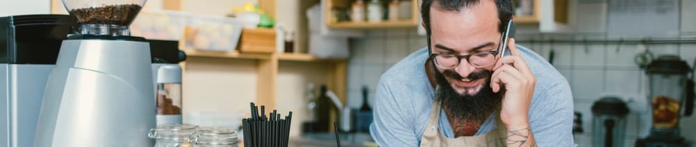 A man leans over a counter, a cell phone held up to his ear.