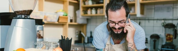 A man leans over a counter, a cell phone held up to his ear.