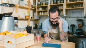 A man leans over a counter, a cell phone held up to his ear.