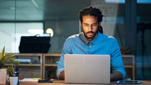 A man uses his laptop while sitting at a desk.