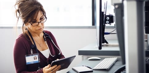 A female doctor looks down at a tablet in her hands.