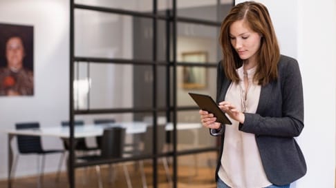 A business woman stands while working on her tablet device.